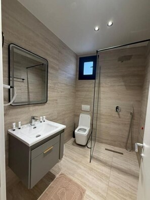 Un baño moderno con un espejo grande, un tocador con lavabo, inodoro y zona de ducha con mampara de vidrio.