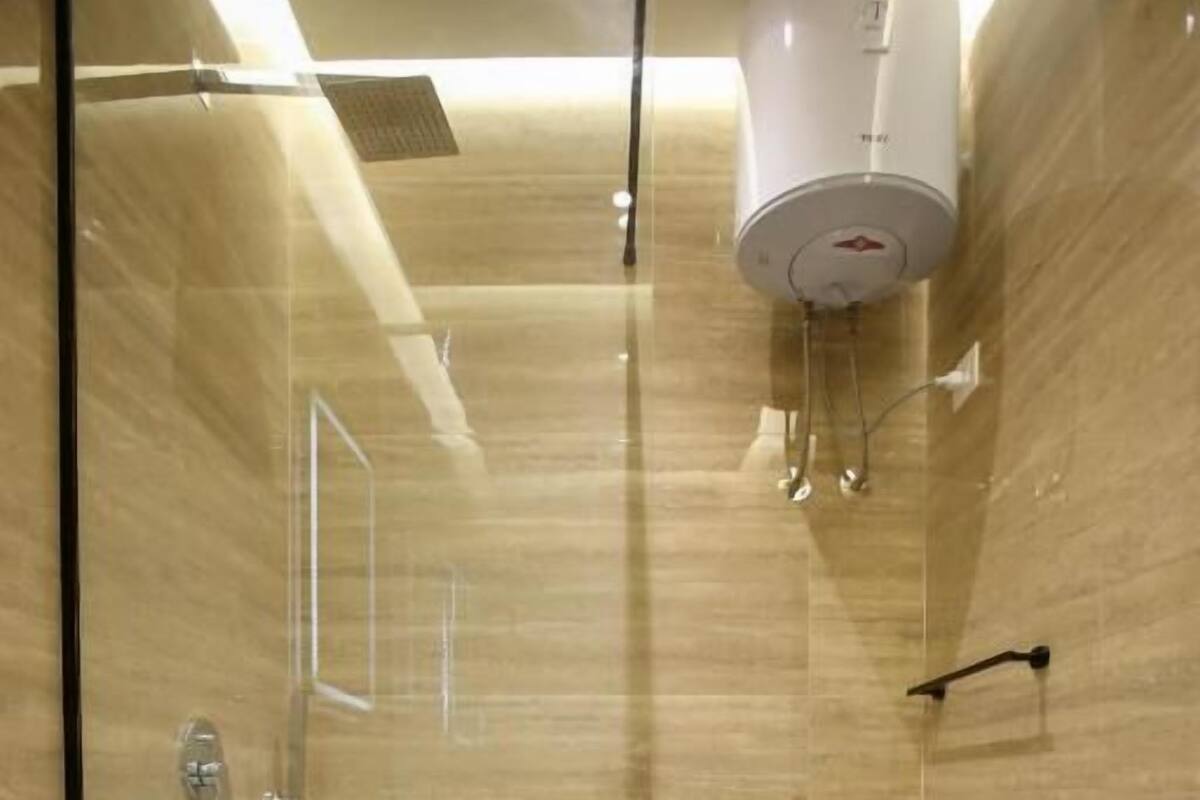 A modern bathroom with a glass shower enclosure, a toilet, and a white heater mounted on the wall.