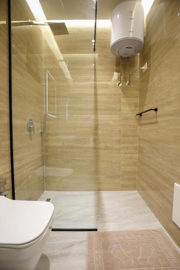 Un baño moderno con cabina de ducha de vidrio, un inodoro y un calentador blanco fijado a la pared.