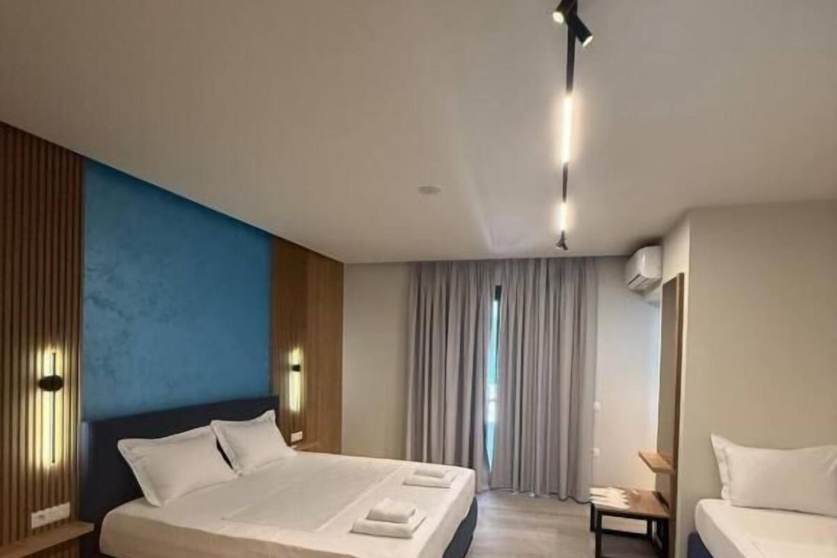 A modern hotel room with a large bed, a smaller bed, a nightstand, and a window with curtains.
