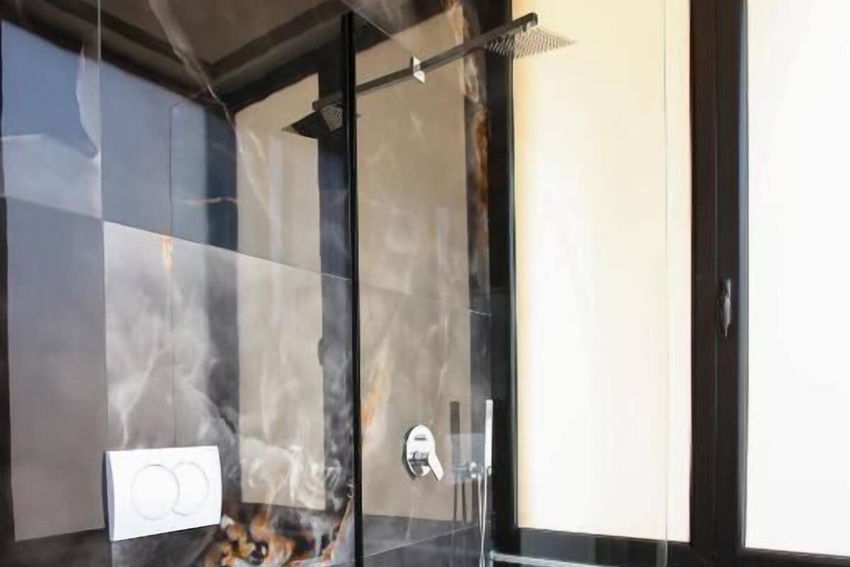 A modern bathroom with a glass-enclosed shower, a white toilet, and a marble backsplash.