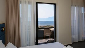 A hotel room with a bed, a chair, and a view of the sea through a large window. - ReiVal Hotel (Vlorë)