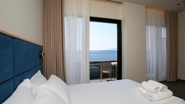 A hotel room with a large bed, a view of the sea, and a balcony with a chair. - ReiVal Hotel (Vlorë)