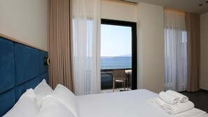 A hotel room with a large bed, a view of the sea, and a balcony with a chair. - ReiVal Hotel (Vlorë)
