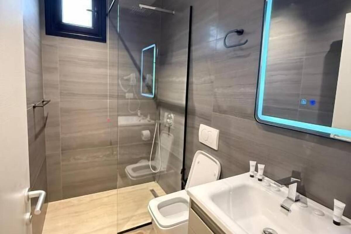 A modern bathroom with a glass shower enclosure, a large mirror, and a vanity with a sink.