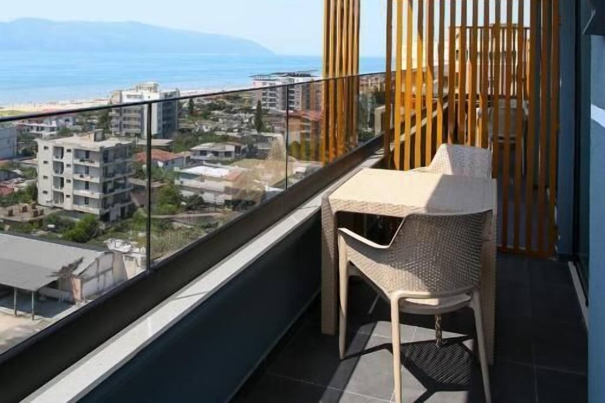 A balcony with a table and chairs, offering a view of the city and the sea.