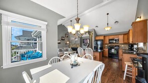A modern kitchen with wooden cabinets, a dining area with a white table, and a view of a house through a large window. - Top-Floor 3BR Ocean City w/ Porch + Parking (Ocean City)