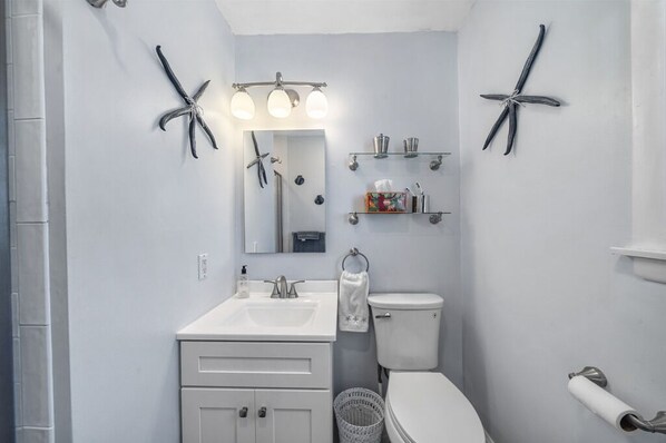 A compact bathroom with a white sink, mirror, and toilet. There are two starfish decorations on the wall, a shelf with toiletries, and a basket near the toilet.
