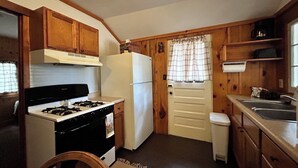 A compact kitchen with wooden cabinets, a gas stove, a white refrigerator, and a sink.