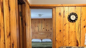 A room with wooden walls, a bed with green bedding, a patterned sofa, and a wall clock.