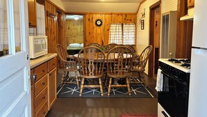 A compact kitchen with wooden cabinets, a dining table with chairs, a microwave, and a stove.
