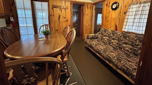 A cozy room with a wooden dining table, chairs, a patterned sofa, and a clock on the wall.
