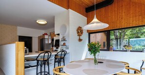 A modern kitchen with white brick walls, wooden ceiling, and a round dining table with a vase of flowers.