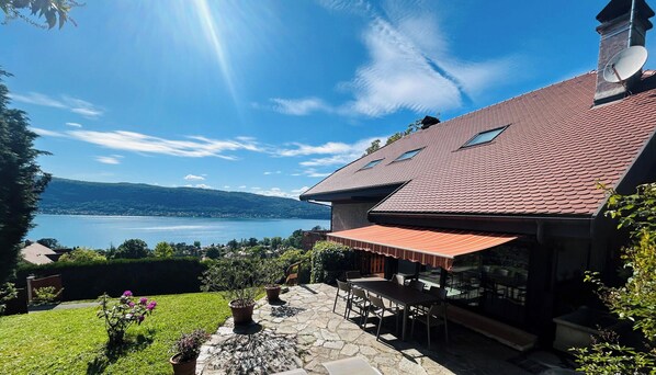 A house with a stone patio, outdoor seating, and a view of a lake.