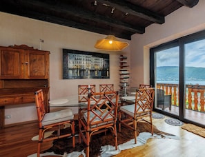 A dining area with a table, chairs, a hanging light fixture, a bookshelf, and a view of the outdoors.