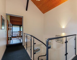 A staircase with a glass railing, a wooden ceiling, and a view of an outdoor seating area.