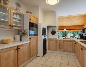 A kitchen with wooden cabinets, a built-in oven, a refrigerator, and a window with a view of trees.