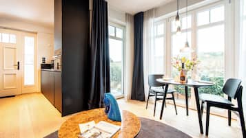 A modern hotel room with a dining area, a kitchen, and large windows offering a view.