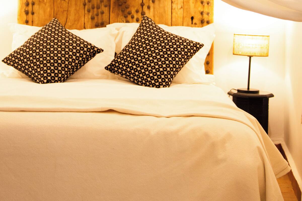 A bed with a wooden headboard, two patterned pillows, and a bedside lamp.
