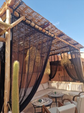 A covered outdoor seating area with a cactus, wooden furniture, and a woven ceiling. - Riad Dar El Mahja (Marrakech)