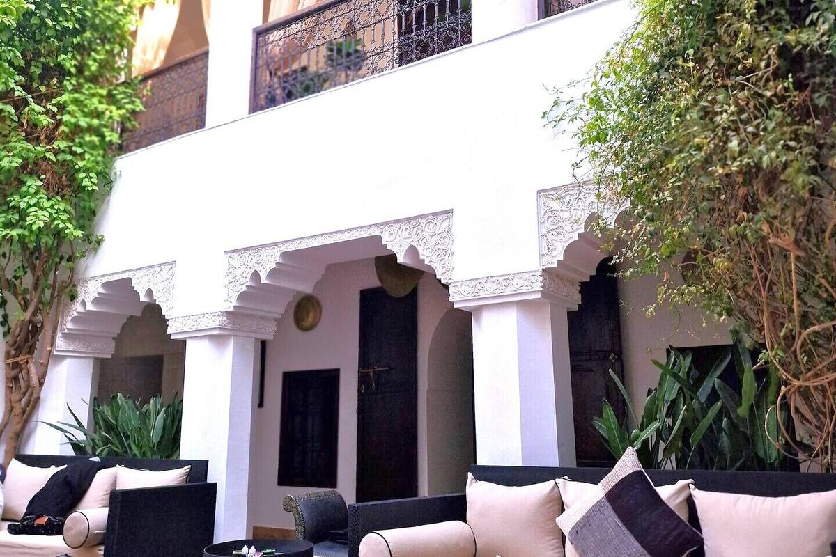 A courtyard with a seating area featuring sofas and ottomans, surrounded by white columns and arches.