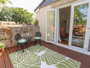 A patio with a table and two chairs, a stone wall, and a sliding glass door leading to an outdoor seating area. - Mount House (Rhyl)