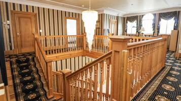 Una habitación amplia con escalera de madera, candelabro y alfombra estampada.