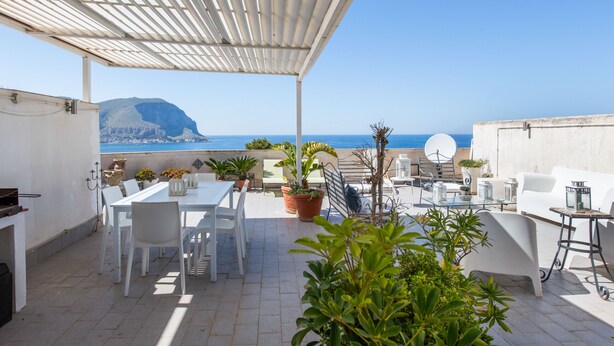 A rooftop terrace with a white table and chairs, potted plants, and a view of the sea and a mountain. - Casa Annibale con Vista Mare by Wonderful Italy (Palermo)