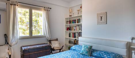 A bedroom with a bed, a bookshelf, a window with curtains, and a wooden chest.