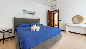 A neatly made bed with a blue bedspread and pillows, a bedside table with a lamp, and a painting on the wall. - Viadelmare Apartment Monopoli 200m Sea (Monopoli)