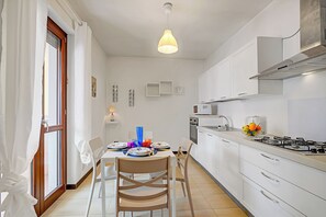 A modern kitchen with white cabinets, a gas stove, and a dining area with a table set for two. - Viadelmare Apartment Monopoli 200m Sea (Monopoli)