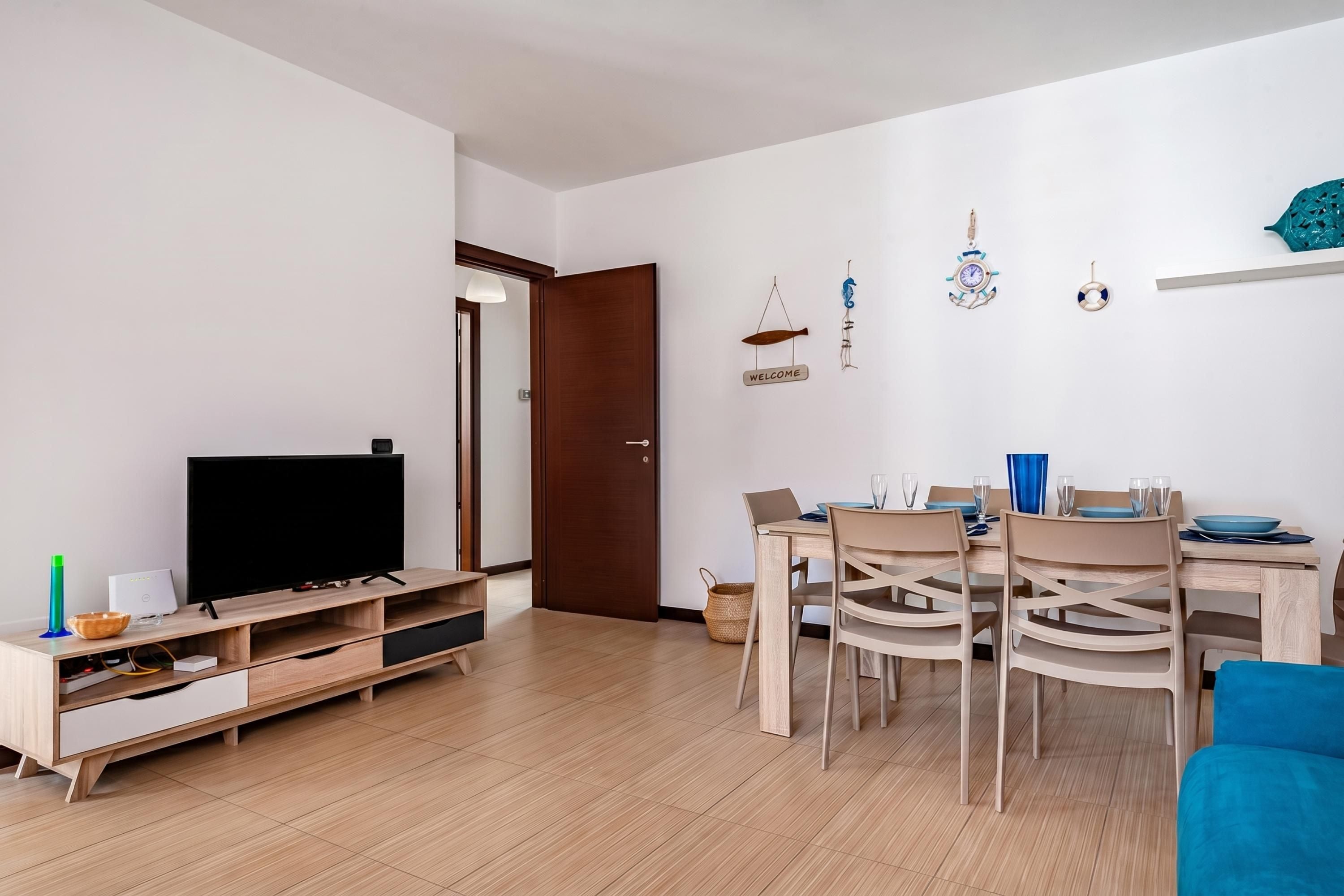 Un salon moderne avec un téléviseur, un meuble de rangement en bois, une table à manger avec des chaises et un canapé bleu.