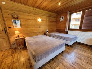 A wooden cabin room with two beds, a nightstand, a lamp, and a poster on the wall.