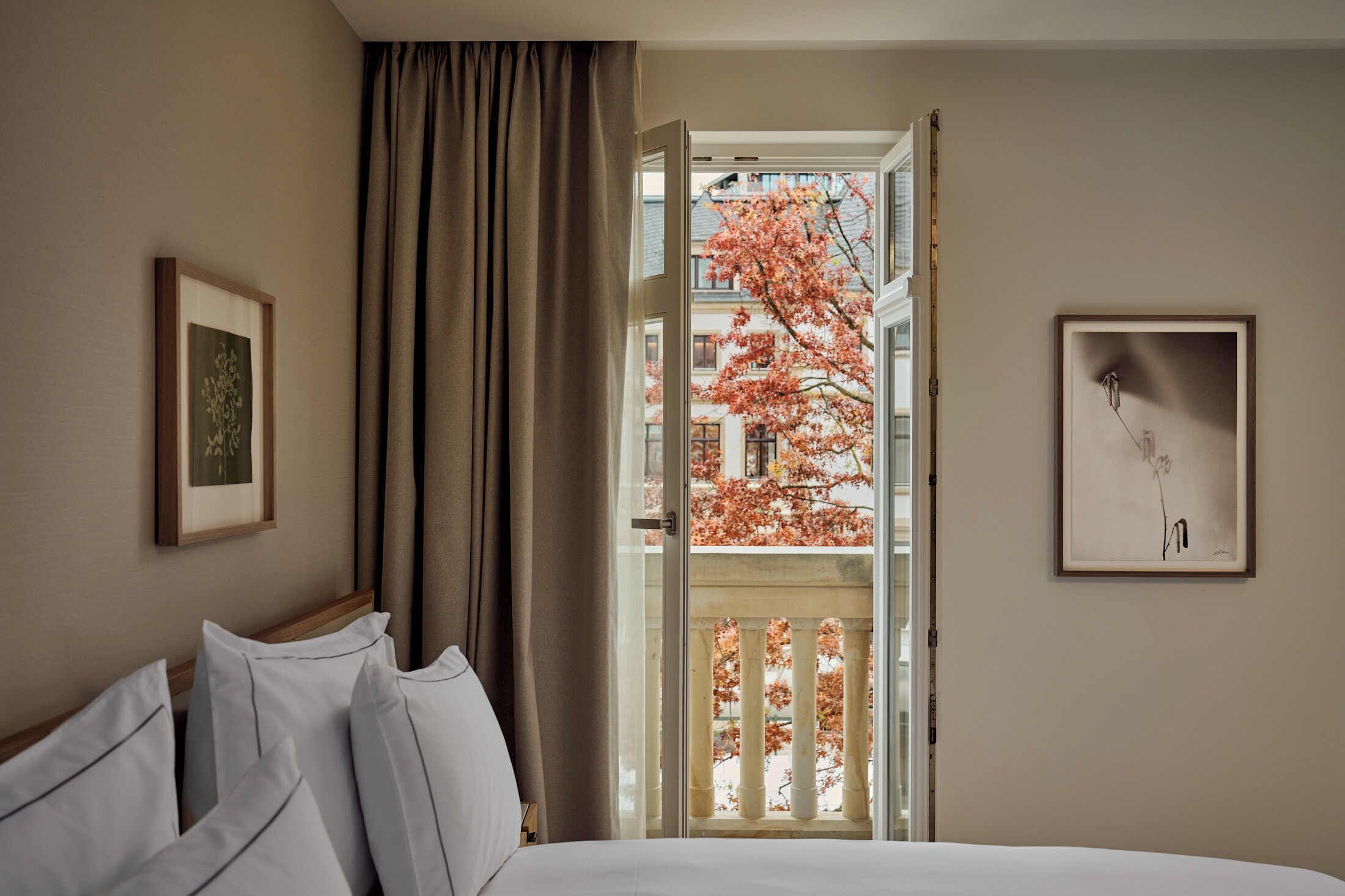 A hotel room with a bed, a window with curtains, and two framed pictures on the walls.