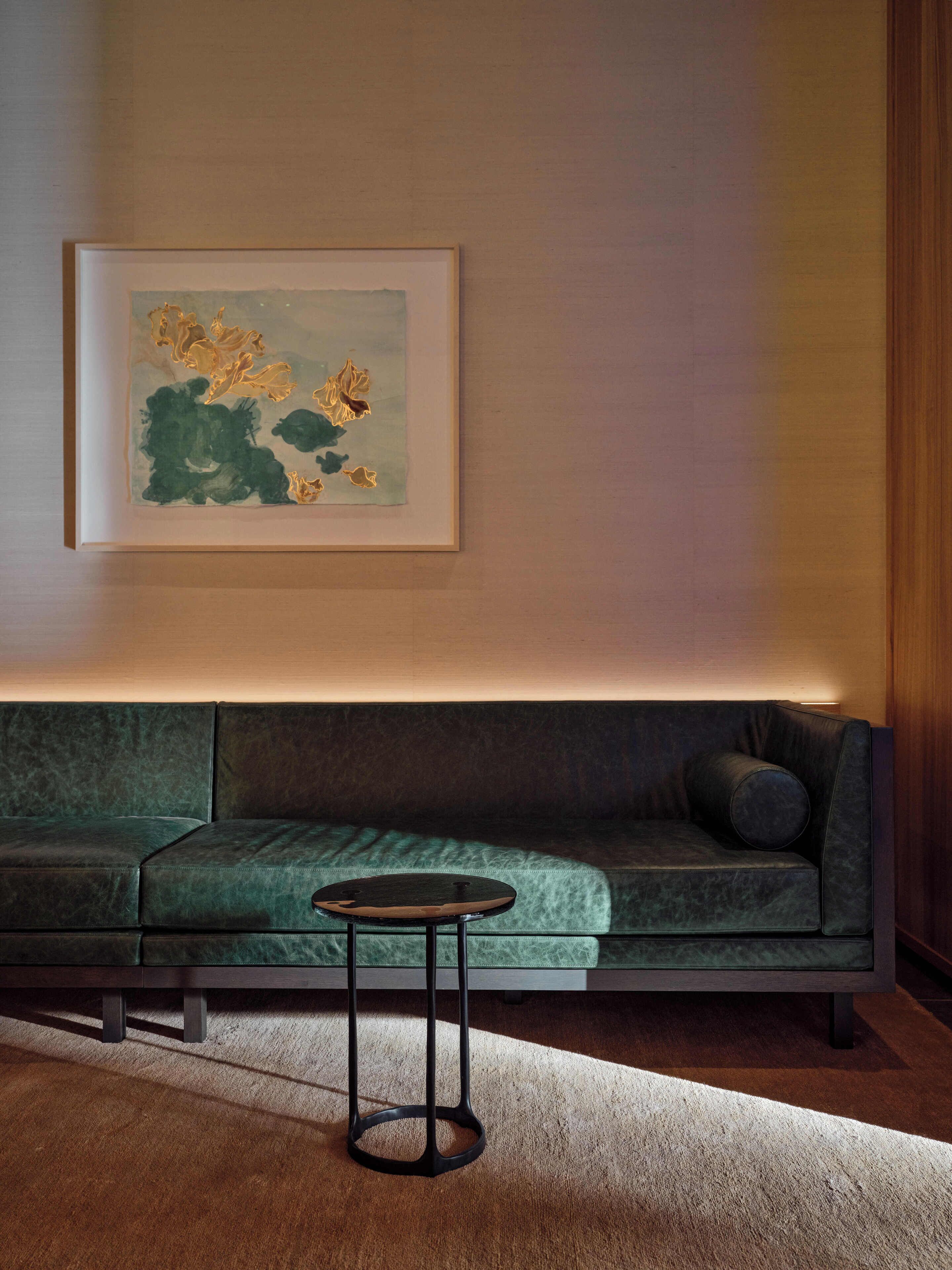 Un salon moderne avec un canapé vert, une petite table ronde et un tableau abstrait encadré accroché au mur.