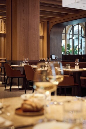 A restaurant with wooden paneling, tables set with wine glasses, and a view through a large arched window. - The Florentin by Althoff Collection (Frankfurt)