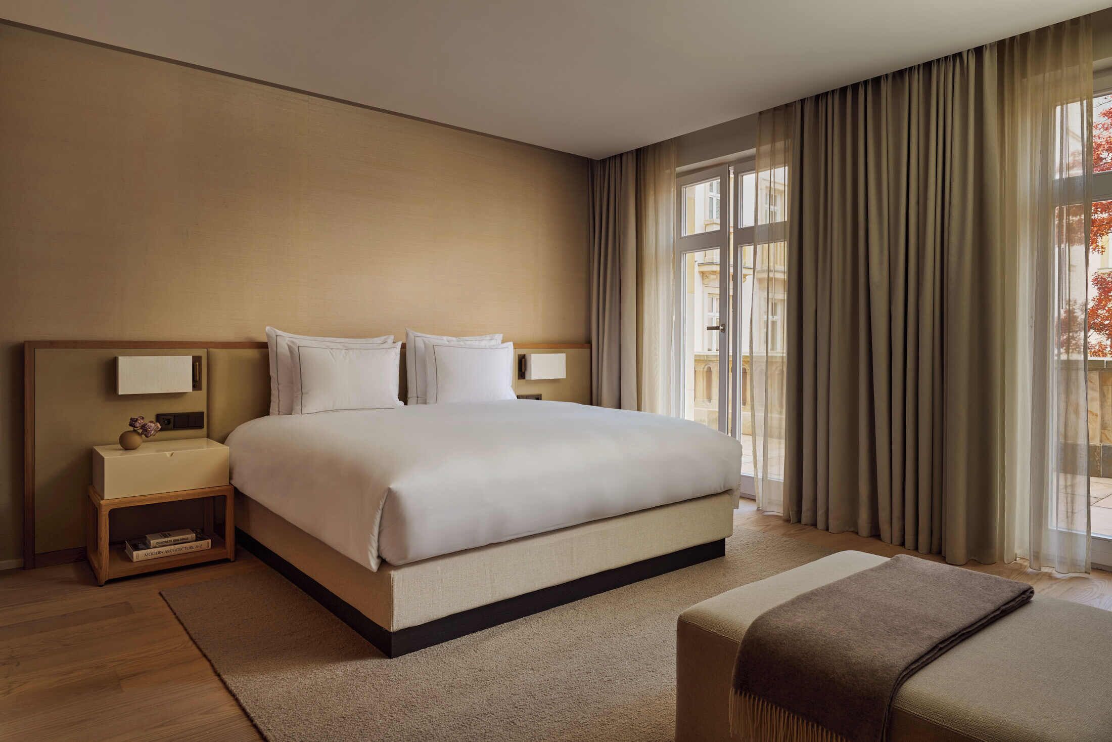 A hotel room with a large bed, bedside tables, and a view of the outdoors.
