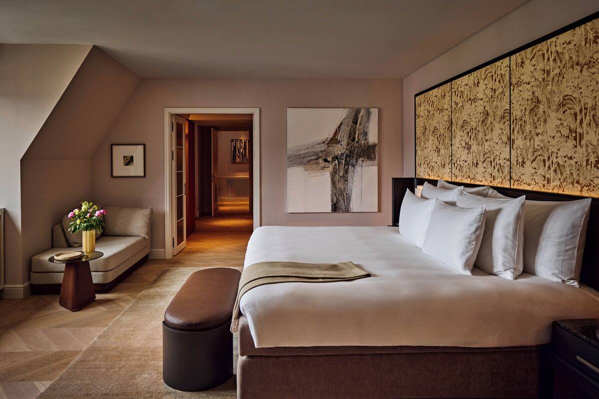 A bedroom with a large bed, a sofa, a small table with flowers, and a painting on the wall.