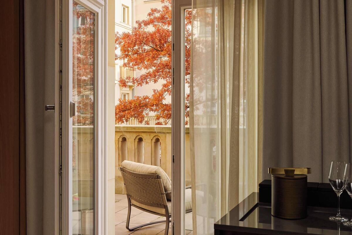 An open sliding glass door leading to a balcony with a chair and a table with a wine glass.