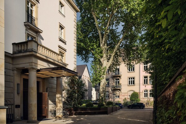 Un edificio de estilo arquitectónico clásico, con columnas, un acceso cubierto y una calle bordeada de árboles.