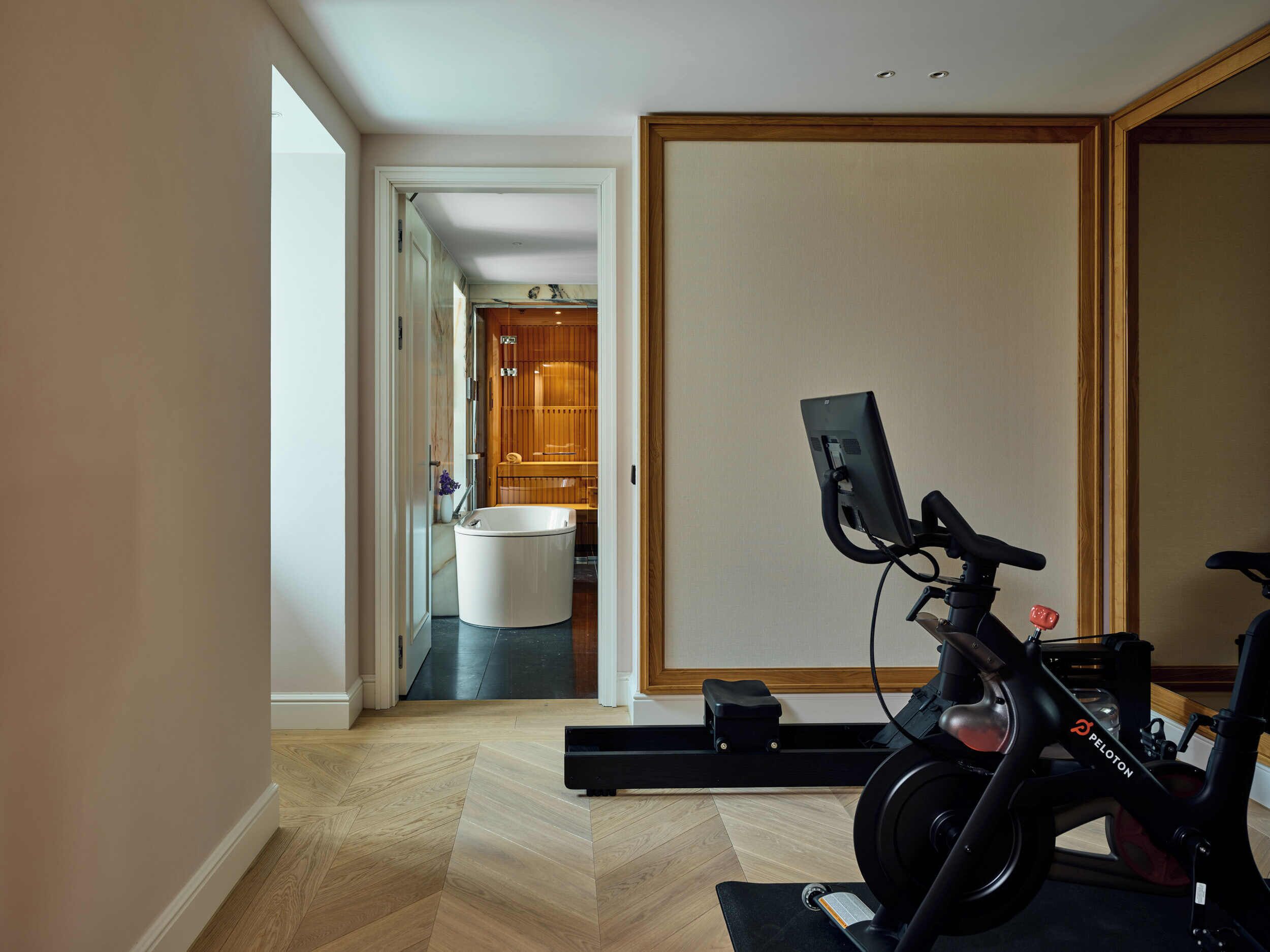 Una habitación moderna con una bicicleta Peloton, un taburete pequeño negro y un armario de madera al fondo.