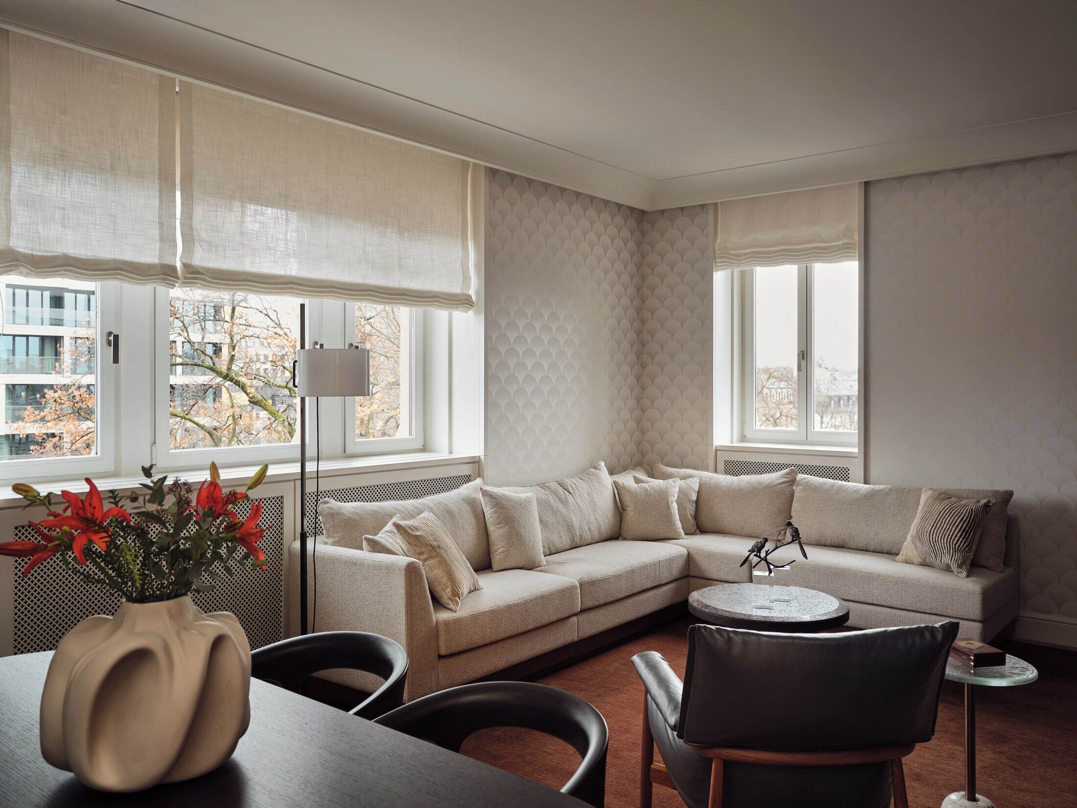 Una sala de estar moderna con un sofá seccional color beige, una mesa redonda y un comedor con una mesa y sillas de madera oscura.