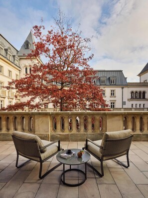 A terrace with wicker chairs and a table, a tree with red leaves, and buildings in the background. - The Florentin by Althoff Collection (Frankfurt)