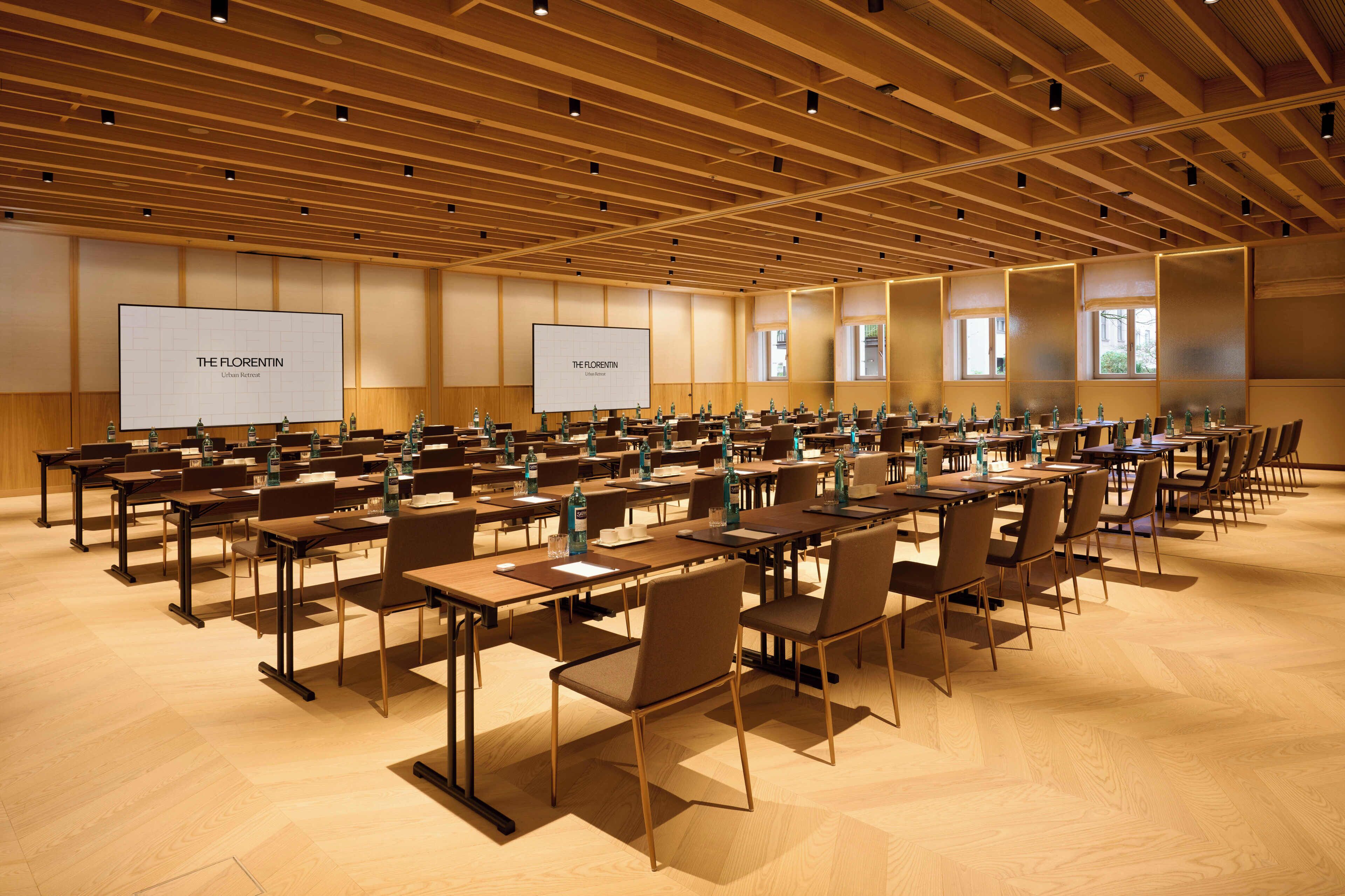 Une salle de conférence dotée de plusieurs tables et chaises, et équipée de projecteurs et d’écrans diffusant des images de « The Florentin Urban Retreat ».