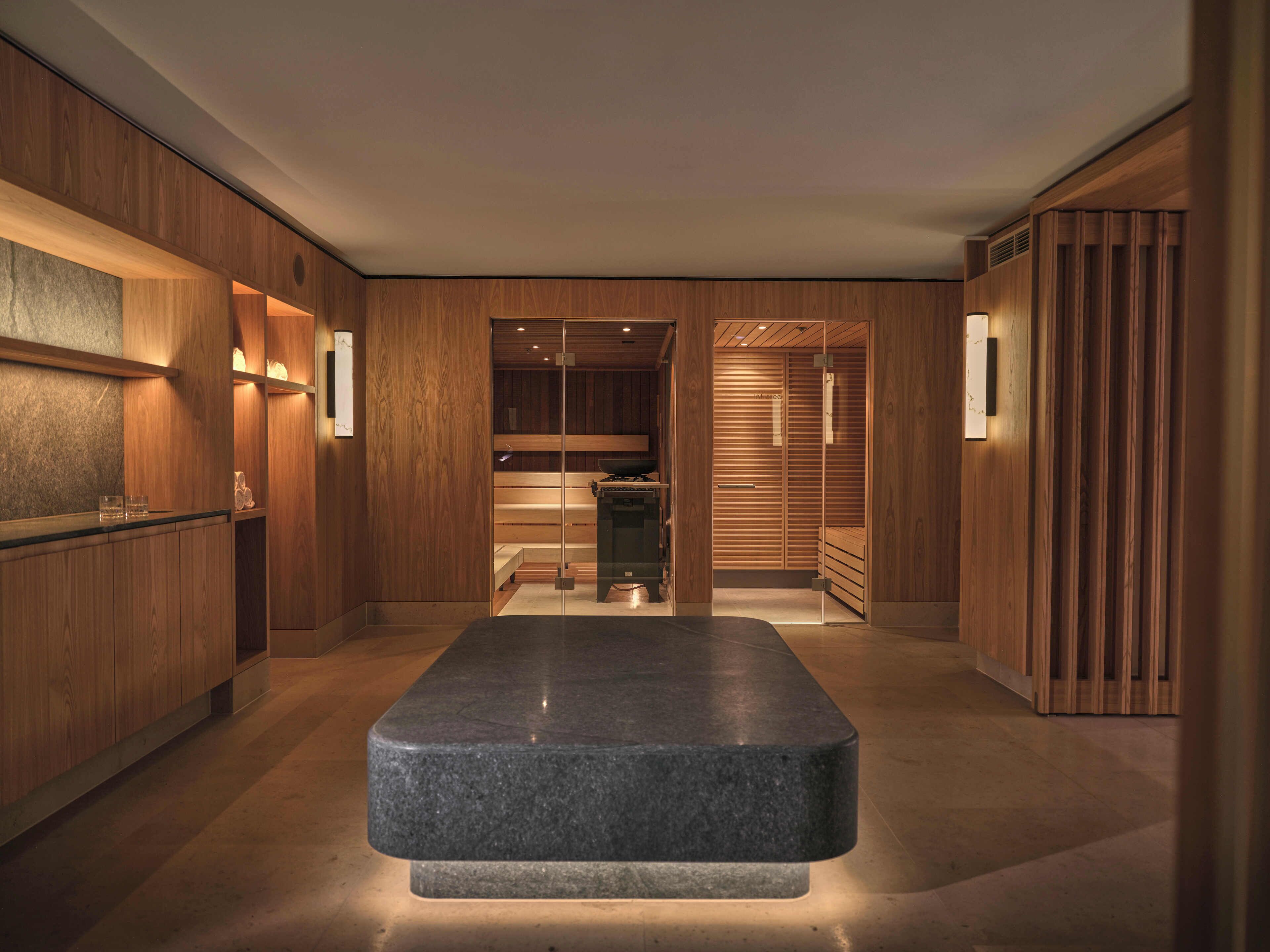 Un interior moderno con paneles de madera, un banco central de piedra y una zona de recepción con mostrador y cristalería.