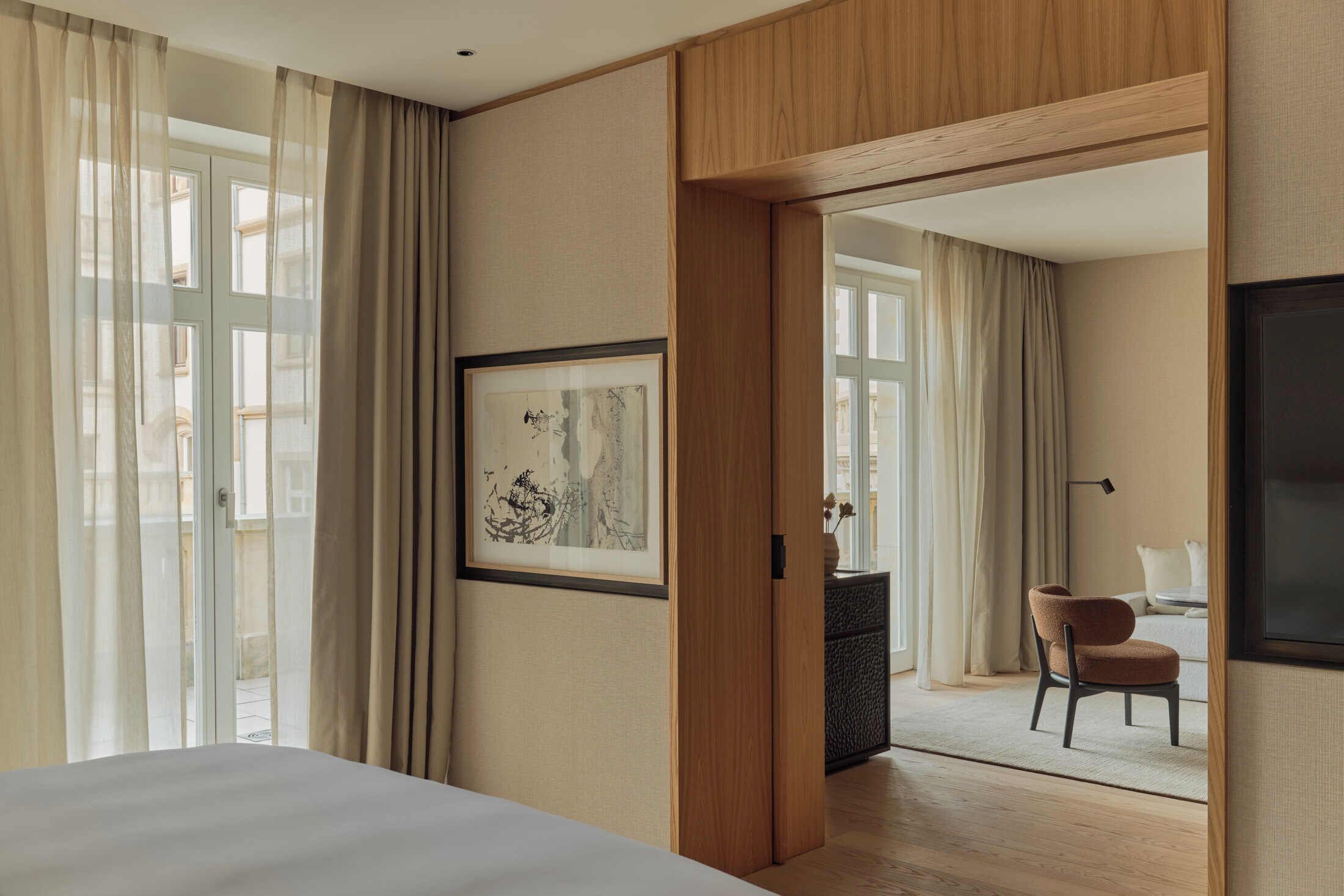 Hotelkamer met een groot bed, een lijst met kunstwerk aan de muur, een houten deur en uitzicht op een balkon met gordijnen.