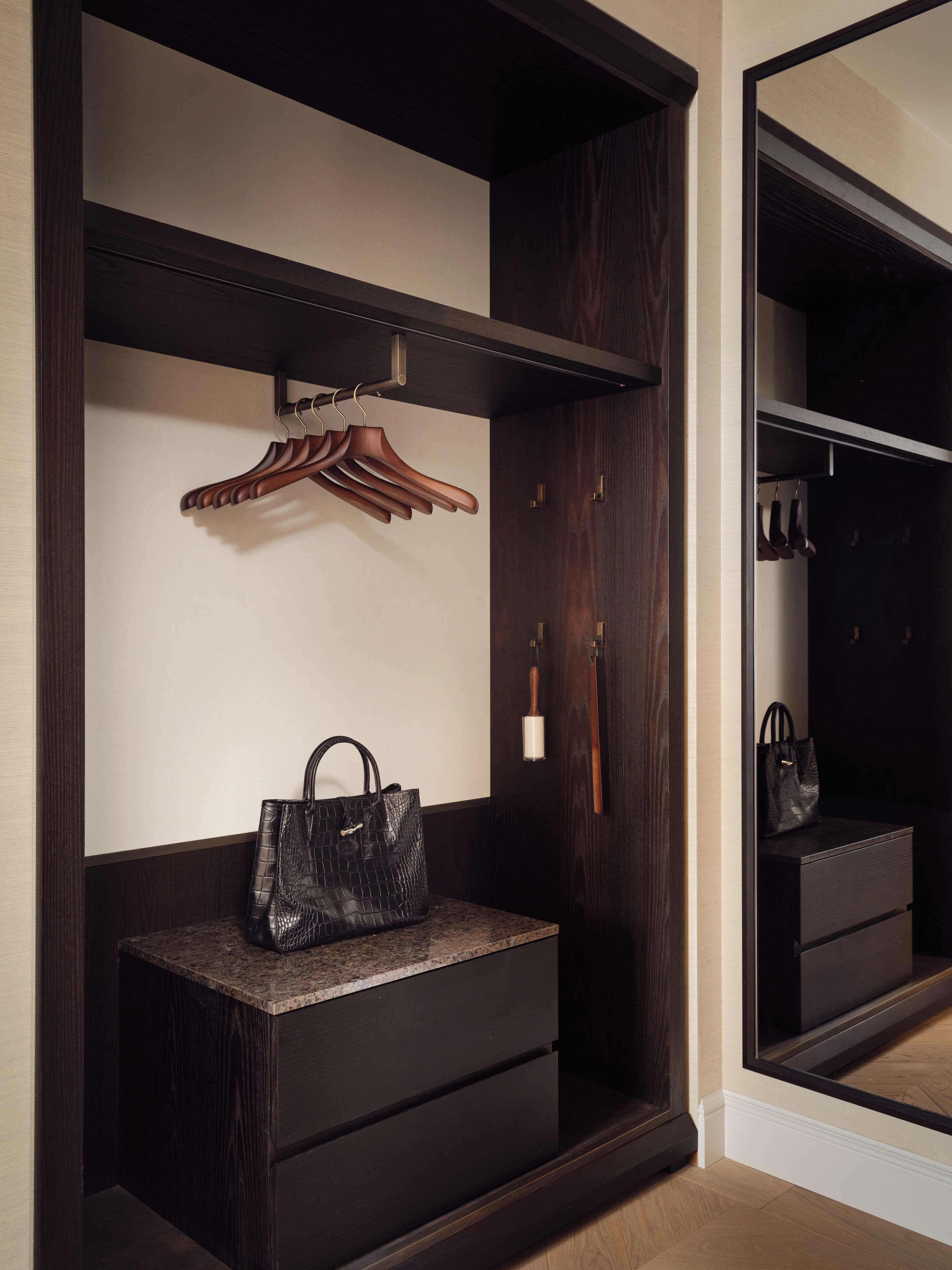 A dark wood wardrobe with a mirror, a wooden hanger, and a black handbag.
