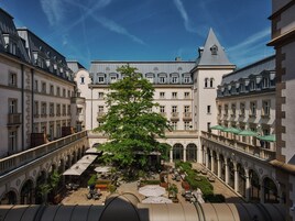 Une cour avec un grand arbre, des sièges extérieurs et un bâtiment doté d’une tour.