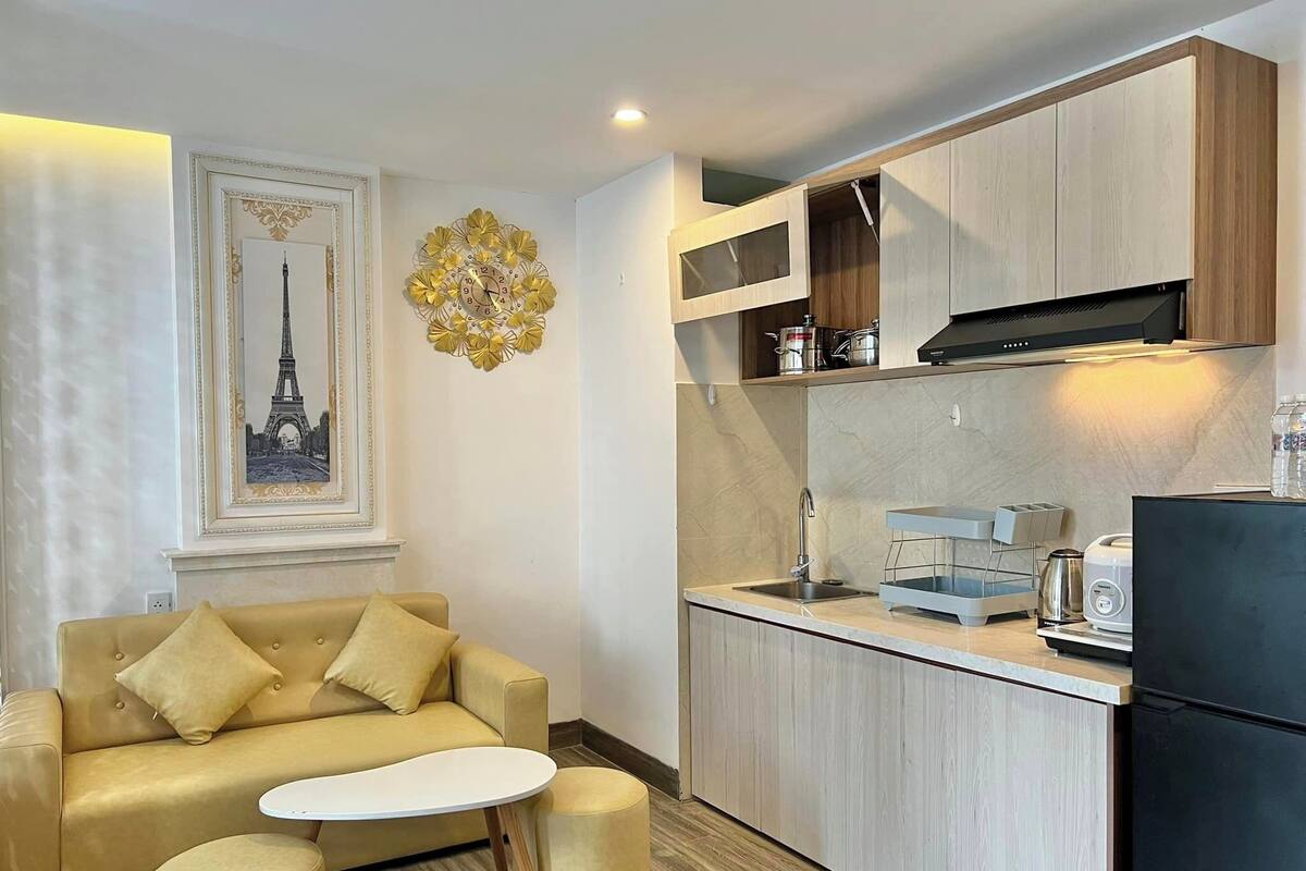 A compact living space with a sofa, a small round table, a kitchen area with cabinets and a refrigerator, and a decorative wall piece.