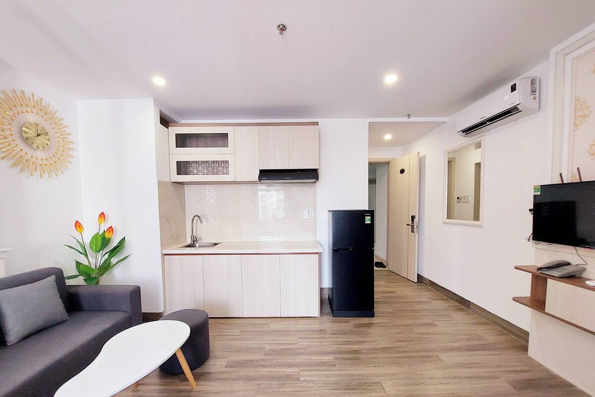 A modern apartment with a kitchen, a living area with a sofa and a coffee table, and a TV on the right.